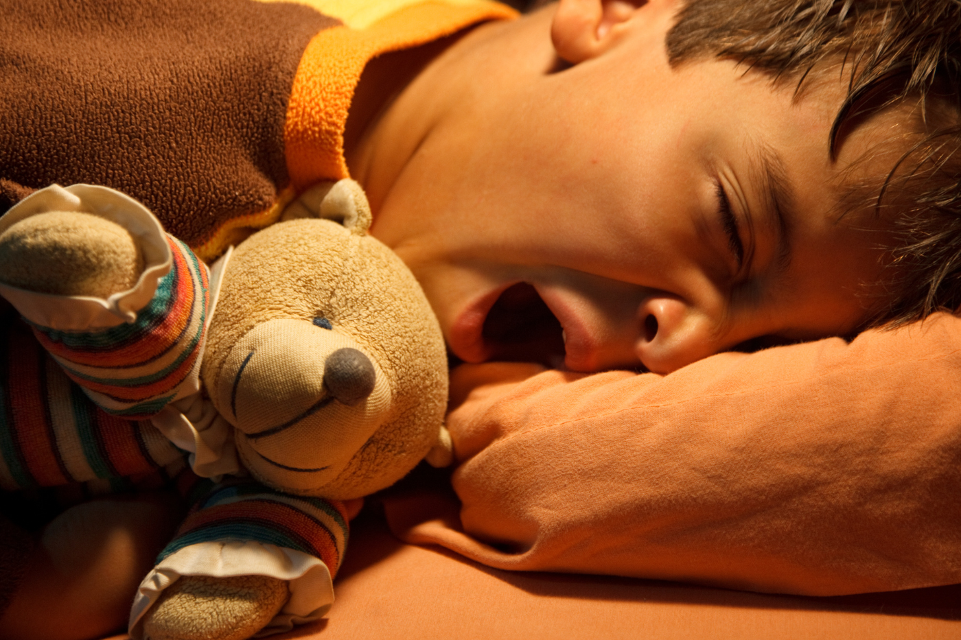 Child yawing on pillow with a teddy bear.